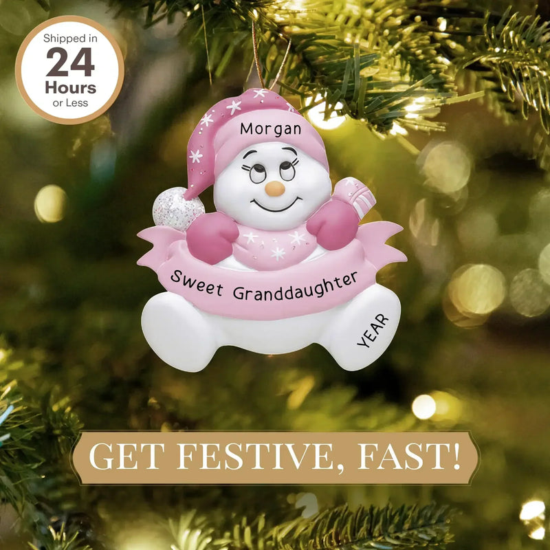MyOrnament pink granddaughter snowman ornament personalized with name and year on a lit Christmas tree.