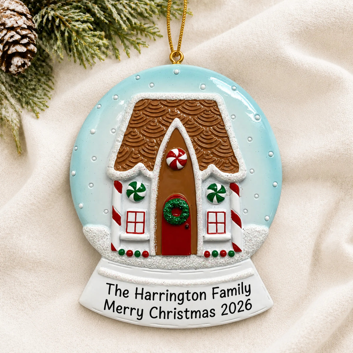 Personalized Gingerbread House Snow Globe christmas ornament laid on a soft white knit blanket