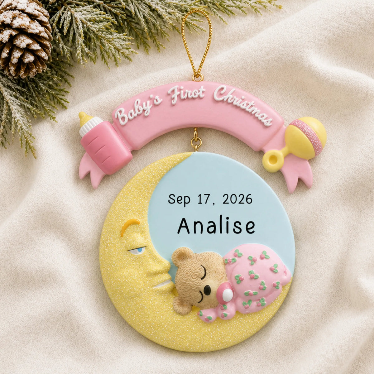 Personalized pink baby's 1st christmas moon ornament laid on a soft white knit blanket