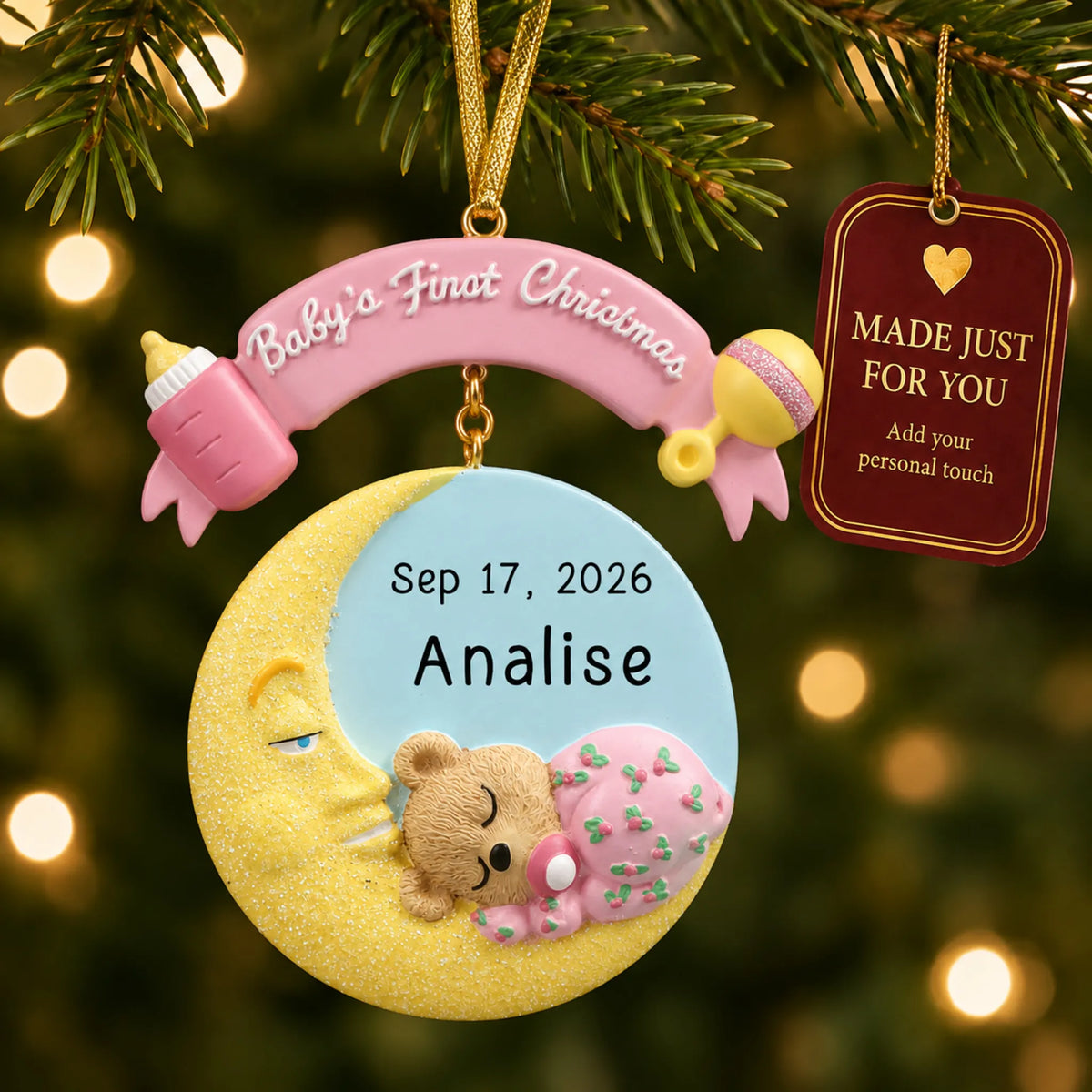 Pink baby's 1st christmas moon ornament hanging on a lit Christmas tree with a Made Just For You gift tag
