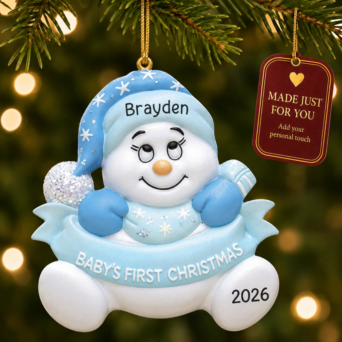 Blue baby's 1st christmas snow baby ornament hanging on a lit Christmas tree with a Made Just For You gift tag