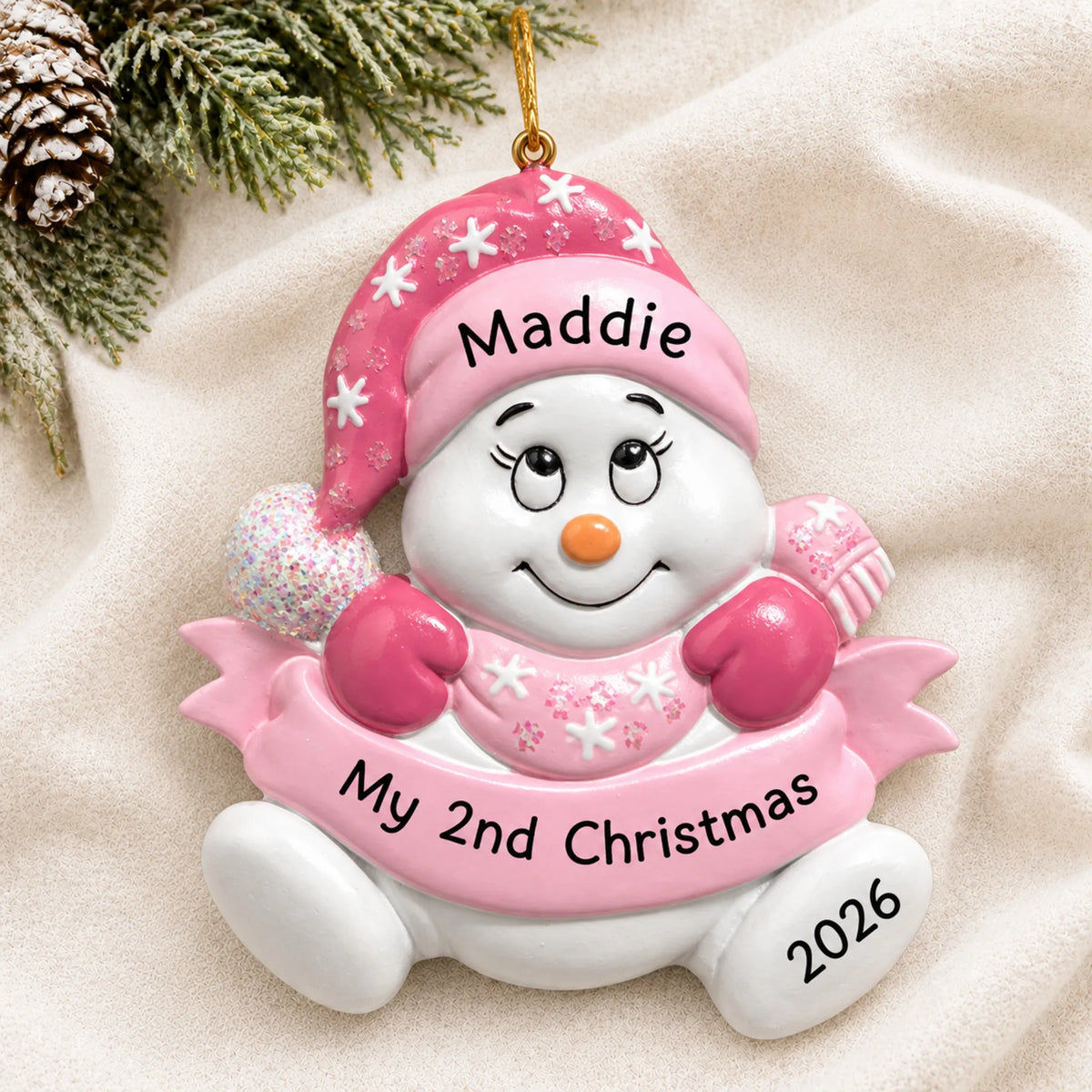 Personalized baby girl 2nd christmas snowman ornament laid on a soft white knit blanket