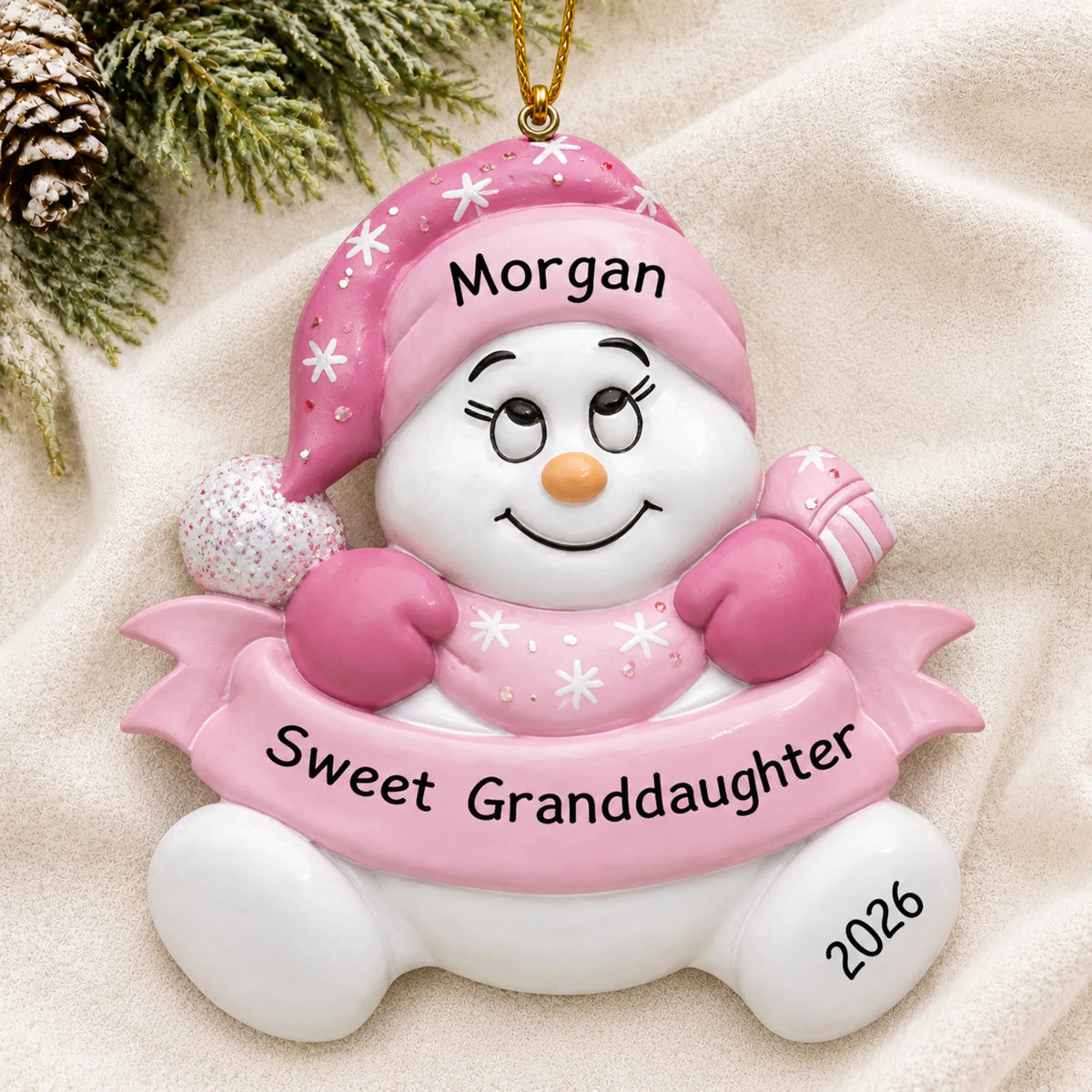 Personalized granddaughter pink snowman christmas ornament laid on a soft white knit blanket