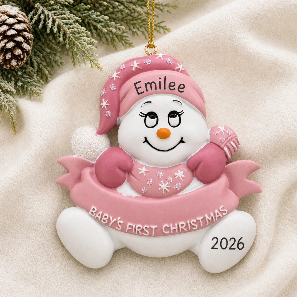 Personalized pink baby's 1st christmas snow baby ornament laid on a soft white knit blanket