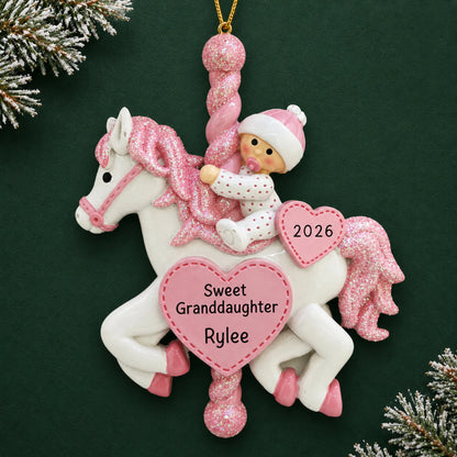 Personalized granddaughter pink baby carousel christmas ornament on a dark green pine background