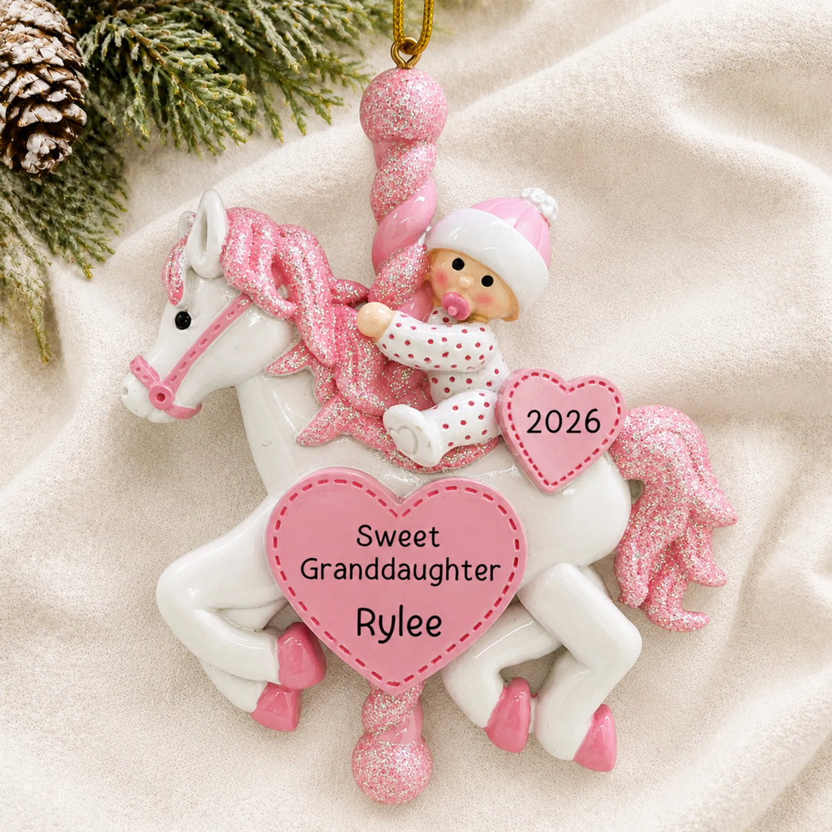 Personalized granddaughter pink baby carousel christmas ornament laid on a soft white knit blanket