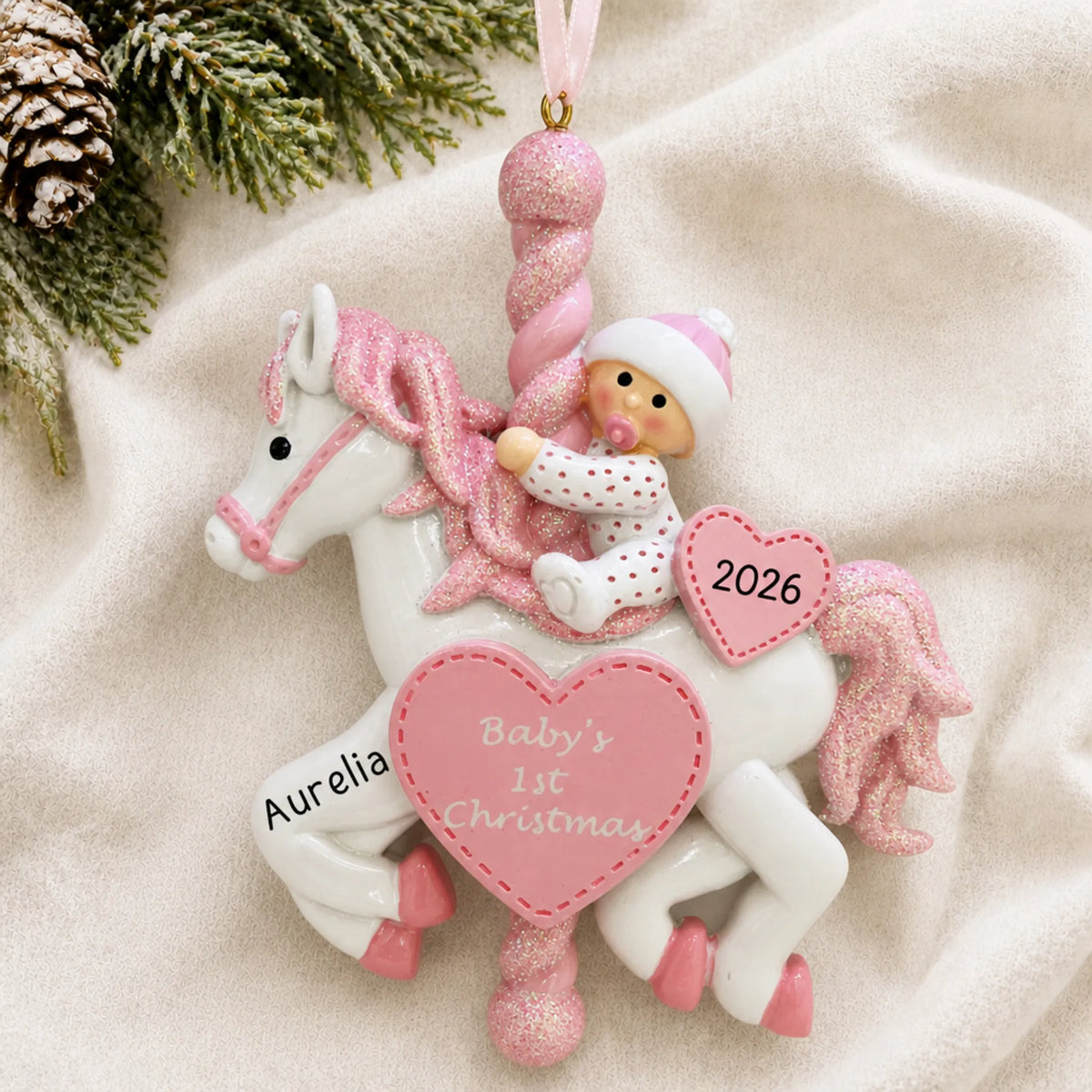 Personalized pink baby's 1st christmas carousel ornament laid on a soft white knit blanket