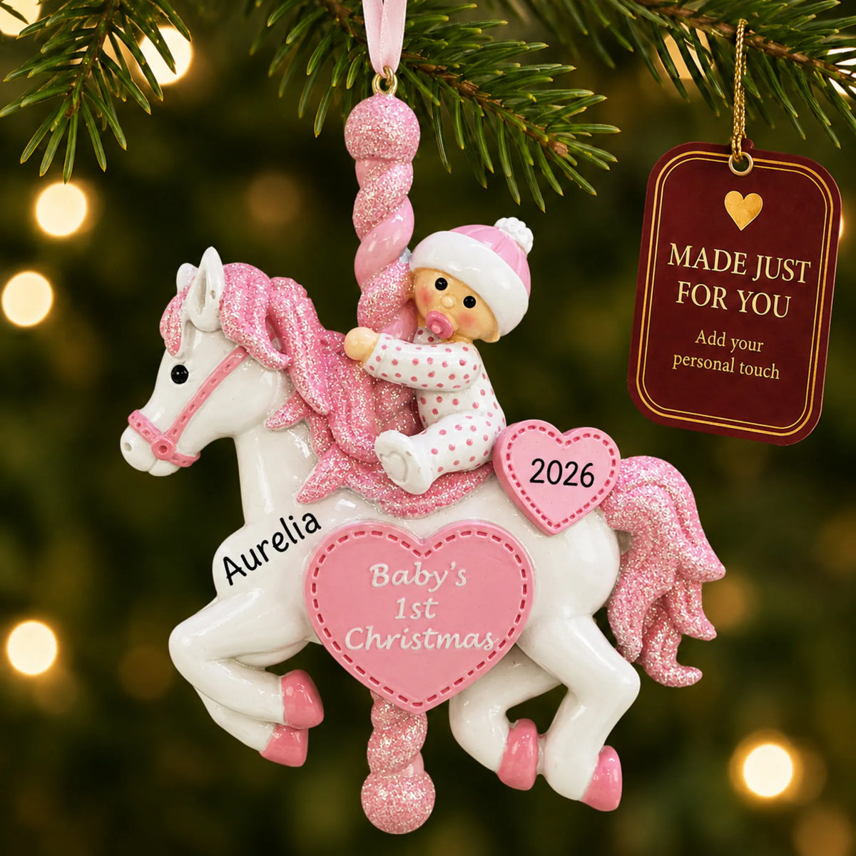 Pink baby's 1st christmas carousel ornament hanging on a lit Christmas tree with a Made Just For You gift tag