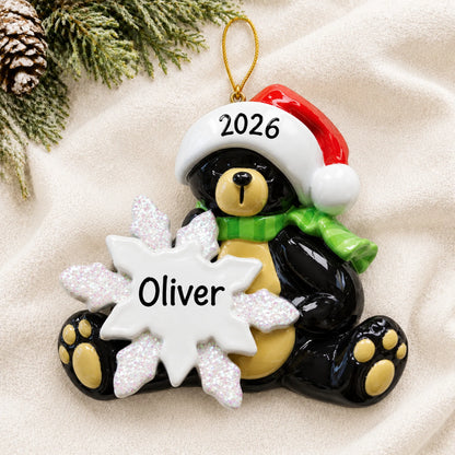 Personalized sitting black bear christmas ornament laid on a soft white knit blanket