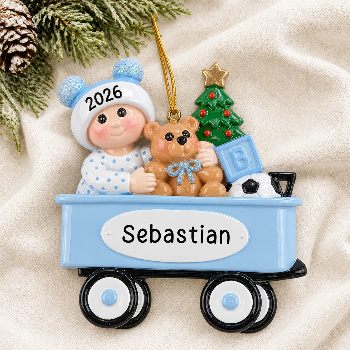 Personalized blue wagon baby boy christmas ornament laid on a soft white knit blanket