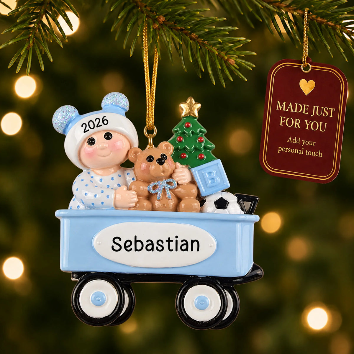 Blue wagon baby boy christmas ornament hanging on a lit Christmas tree with a Made Just For You gift tag