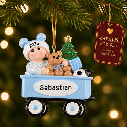 Blue wagon baby boy christmas ornament hanging on a lit Christmas tree with a Made Just For You gift tag
