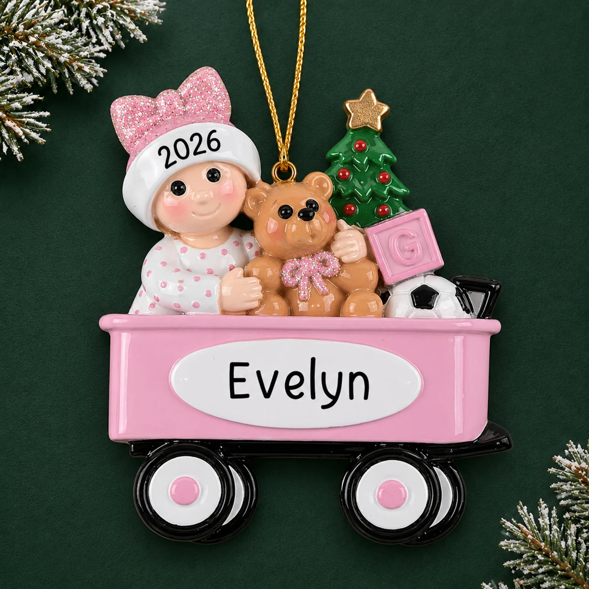 Personalized pink wagon baby girl christmas ornament on a dark green pine background