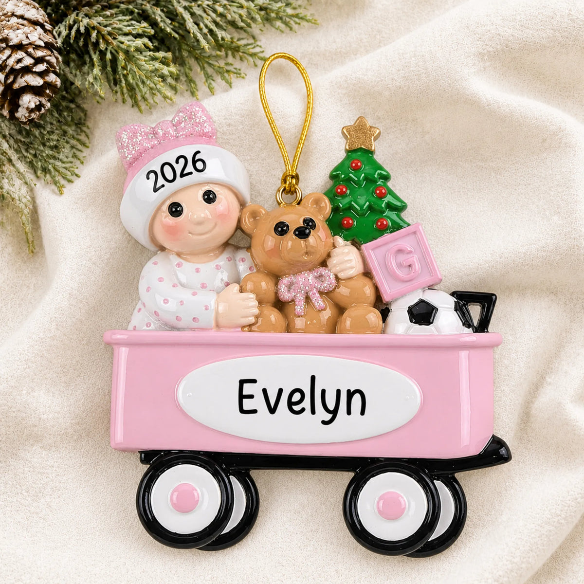 Personalized pink wagon baby girl christmas ornament laid on a soft white knit blanket