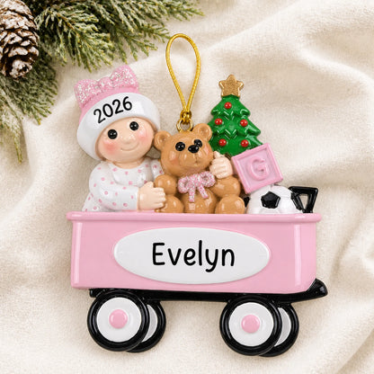 Personalized pink wagon baby girl christmas ornament laid on a soft white knit blanket