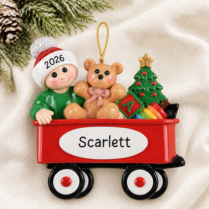 Personalized red wagon baby christmas ornament laid on a soft white knit blanket