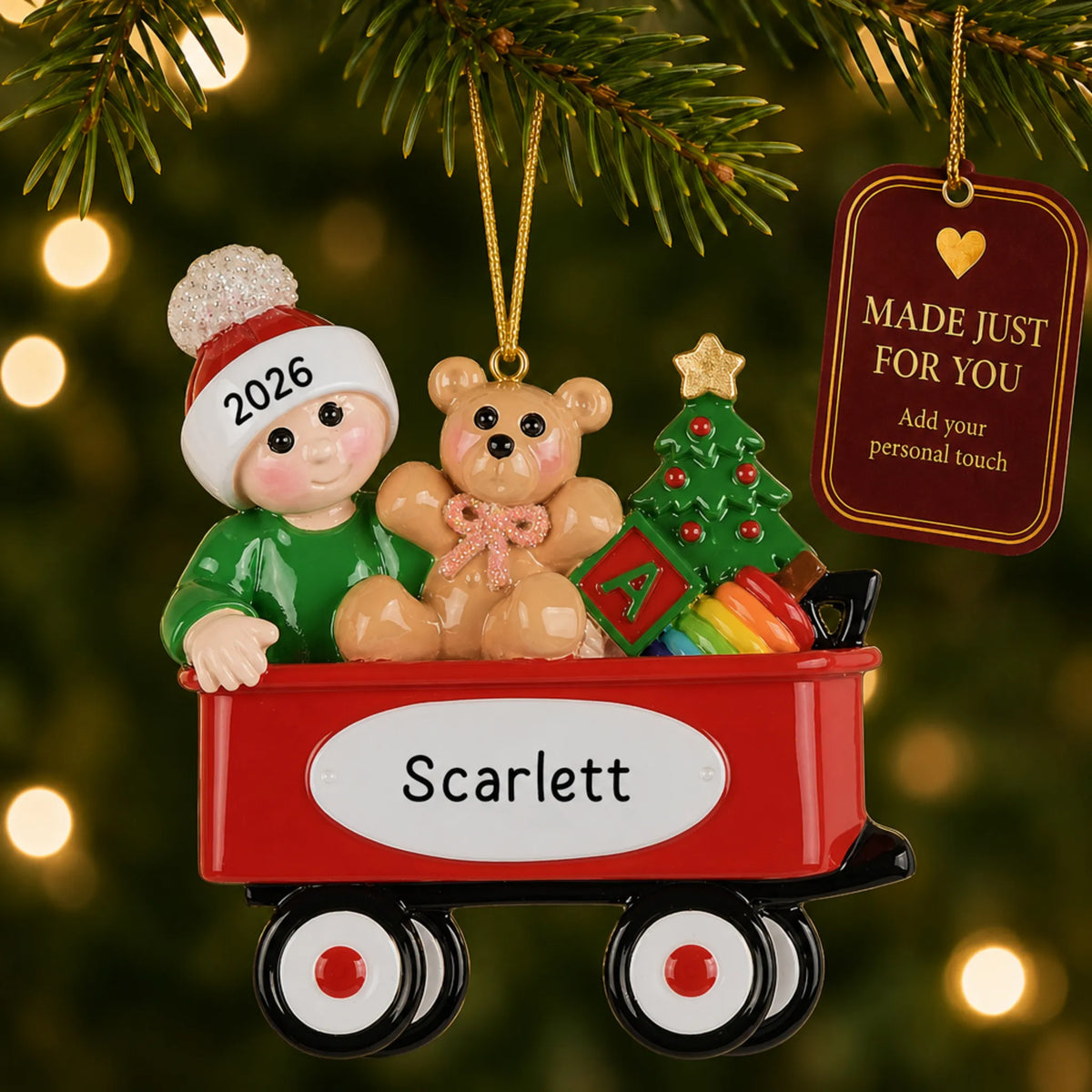 Red wagon baby christmas ornament hanging on a lit Christmas tree with a Made Just For You gift tag