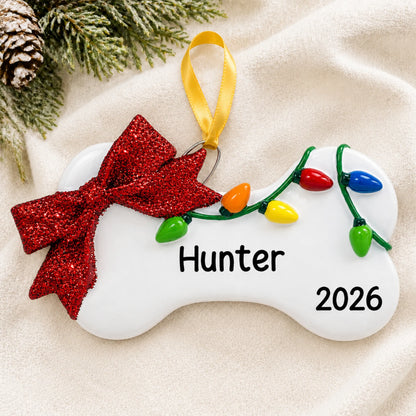 Personalized Holiday Lights Dog Bone christmas ornament laid on a soft white knit blanket