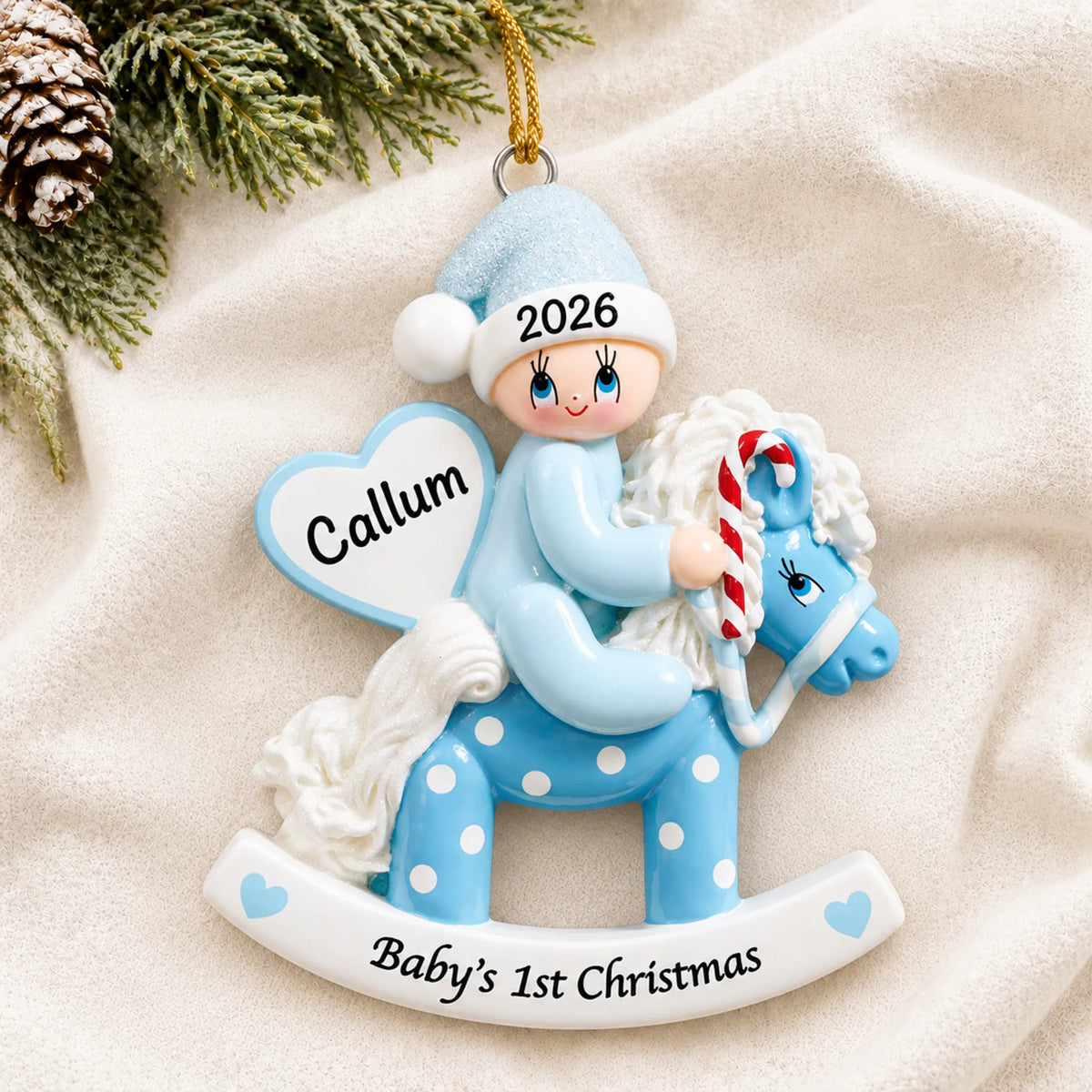 Personalized blue baby's 1st christmas rocking horse ornament laid on a soft white knit blanket