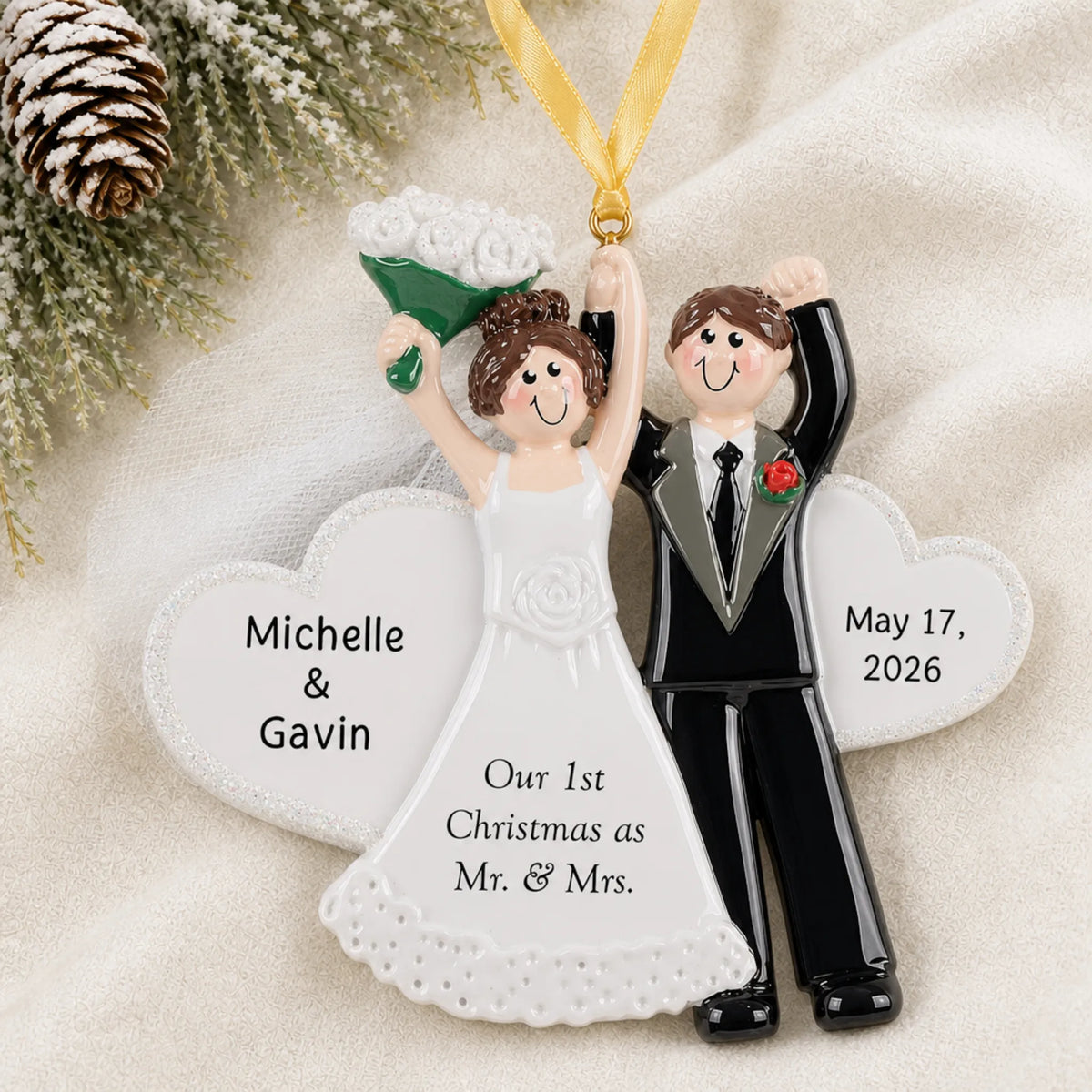 Personalized wedding day Christmas ornament on a cream knit blanket beside pine and pinecones