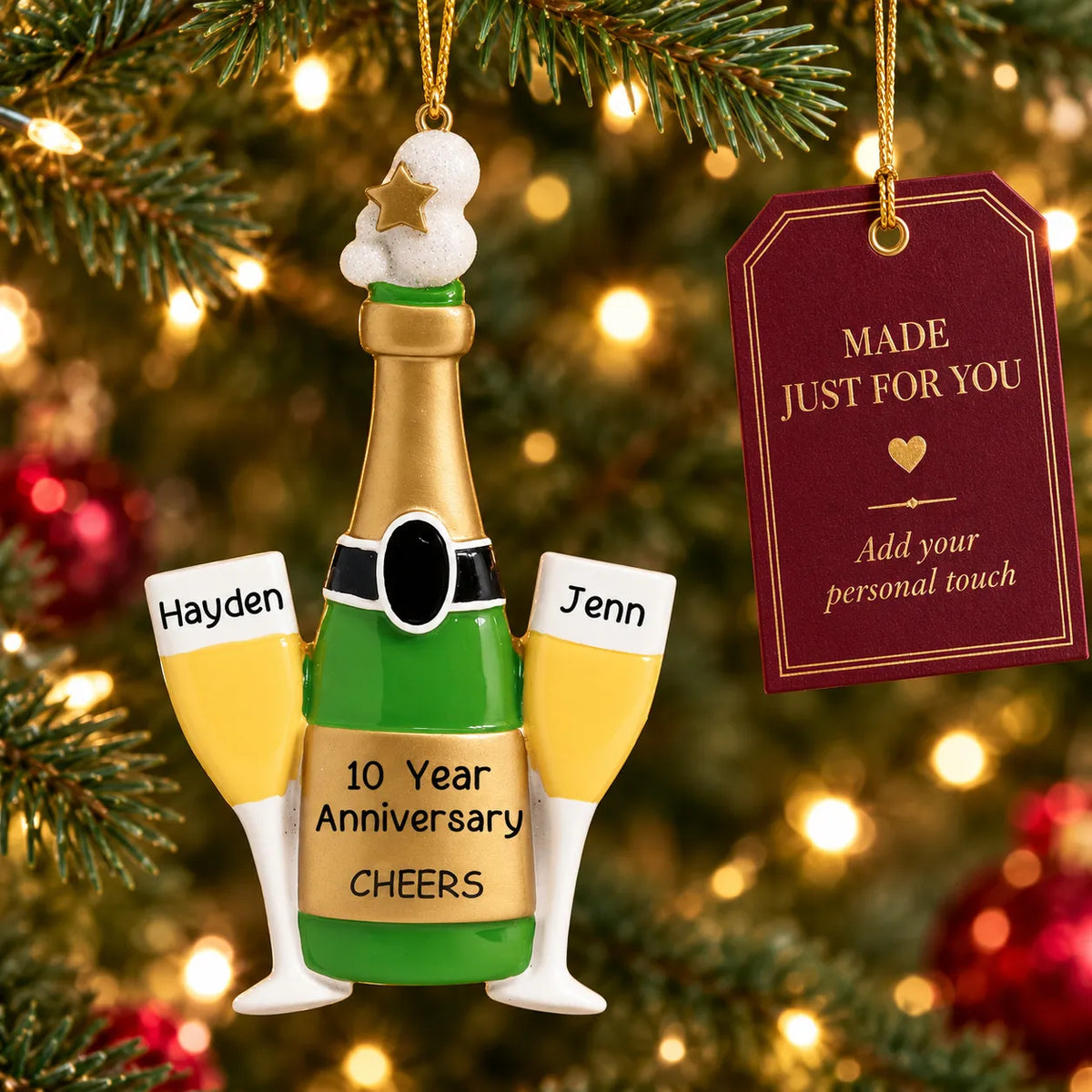 Personalized champagne anniversary Christmas ornament hanging on a lit Christmas tree beside a Made Just For You gift tag