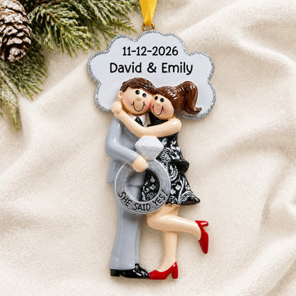 Personalized She Said Yes brunette couple Christmas ornament on a cream knit blanket beside pine and pinecones