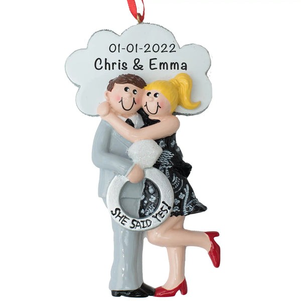 A personalized engagement Christmas ornament featuring a blonde haired couple in a white and black dress holding a ring, with the text 'She Said Yes!' 