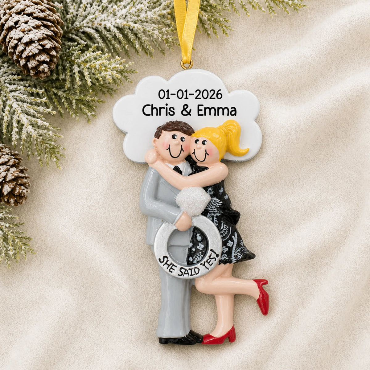 Personalized She Said Yes blonde couple Christmas ornament on a cream knit blanket beside pine and pinecones
