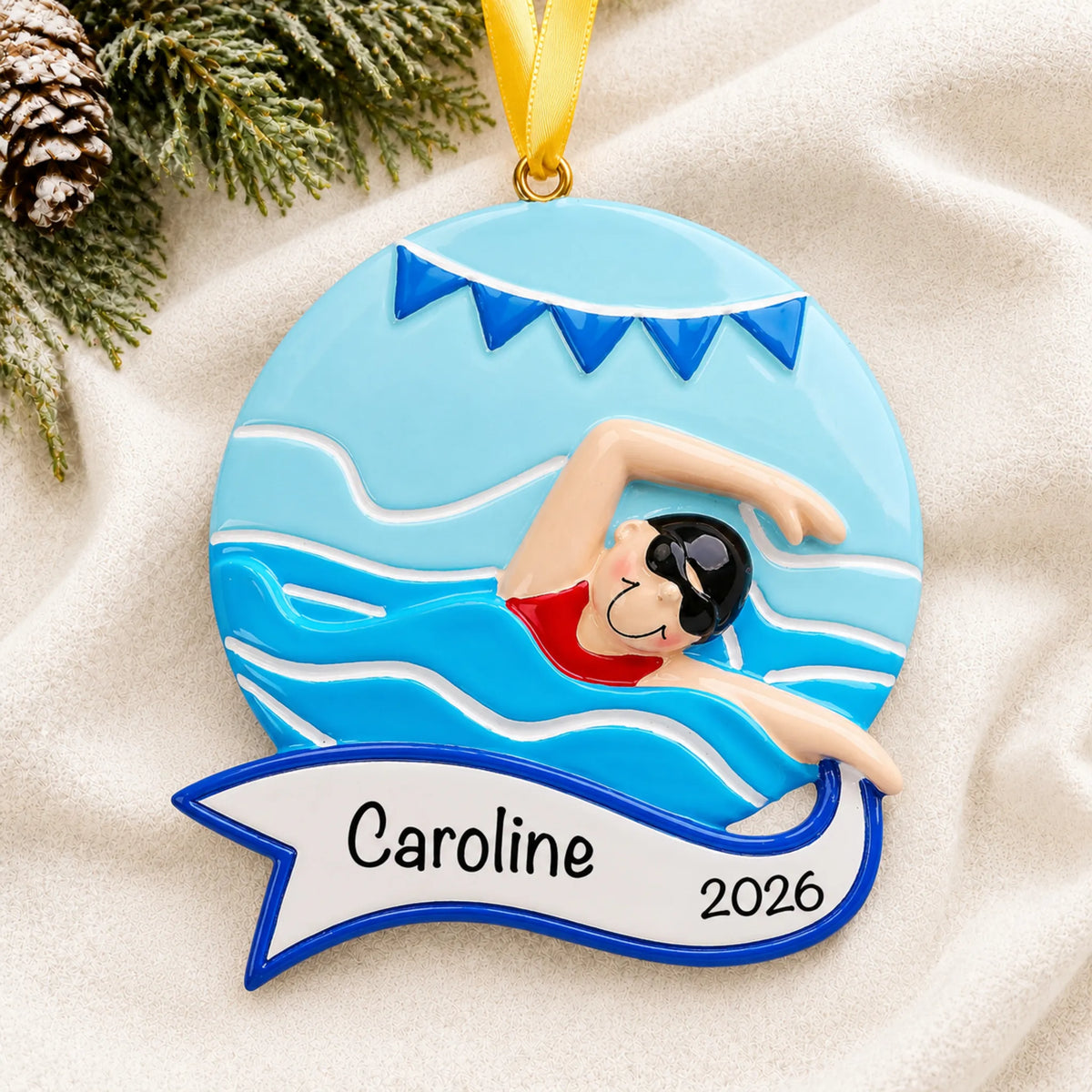 Personalized girl swimming mid-stroke christmas ornament laid on a soft white knit blanket