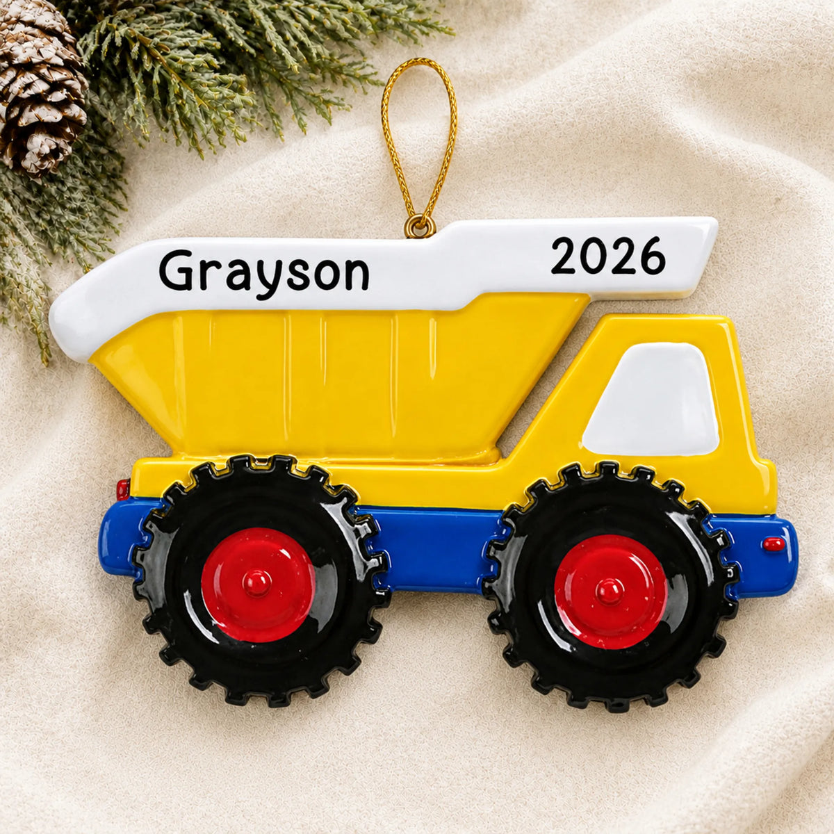 Personalized yellow kids dump truck christmas ornament laid on a soft white knit blanket
