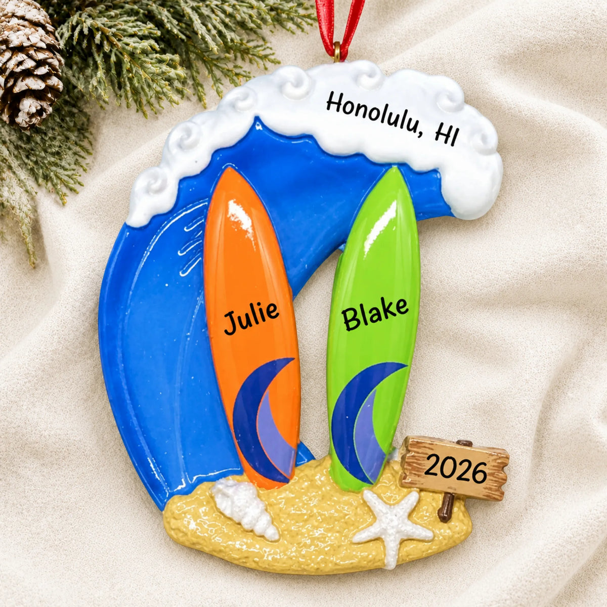 Personalized big wave surfing couple christmas ornament laid on a soft white knit blanket