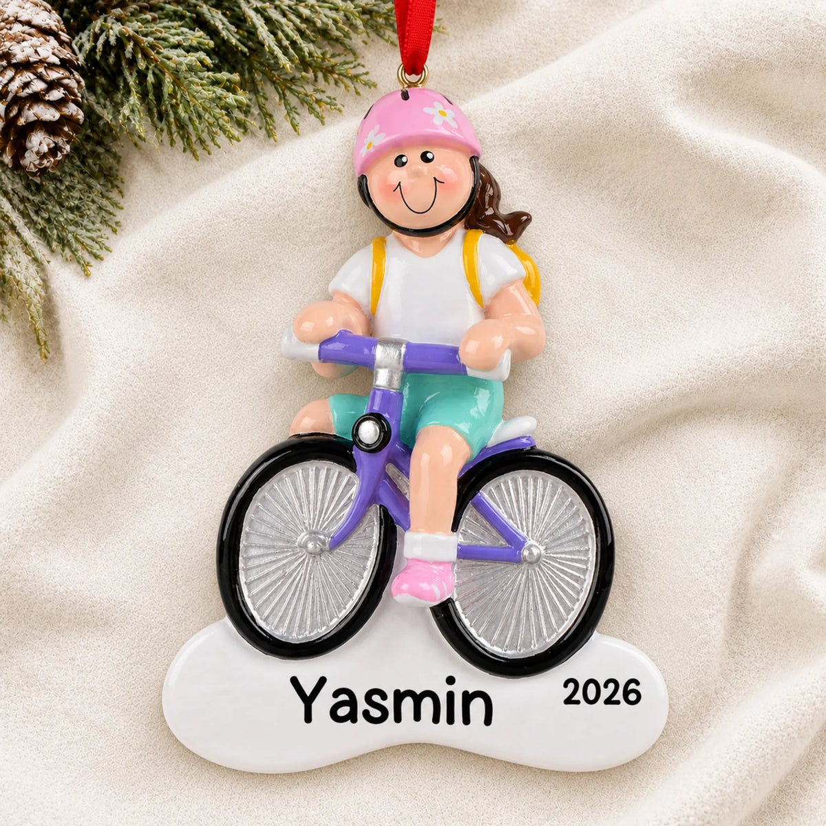 Personalized brunette girl bike christmas ornament laid on a soft white knit blanket