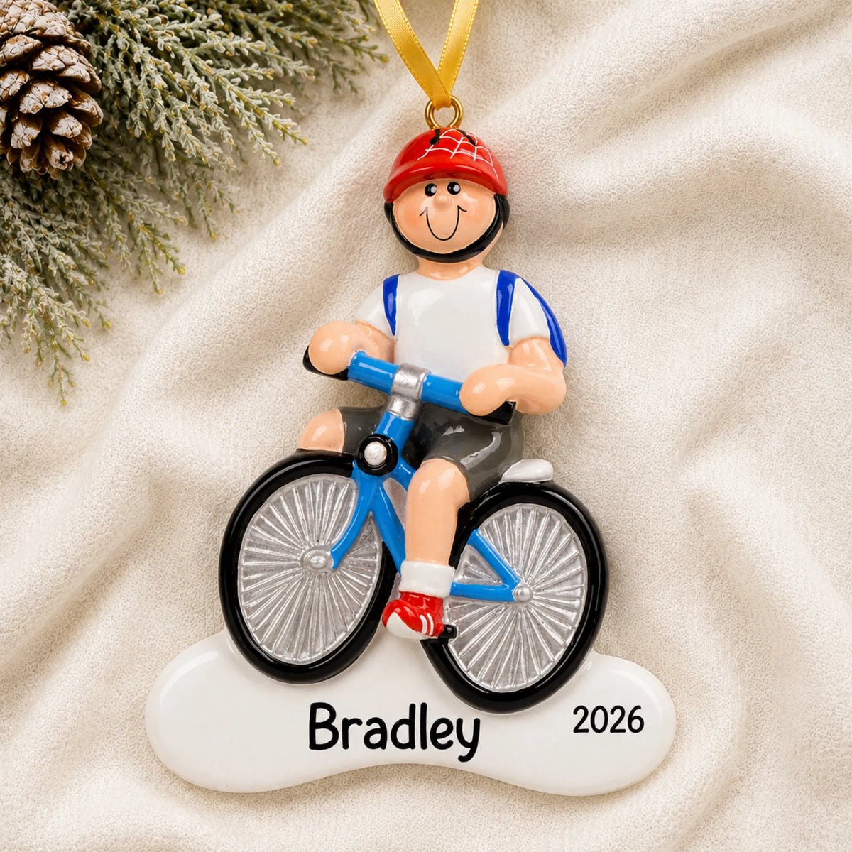Personalized boy riding a bike christmas ornament laid on a soft white knit blanket