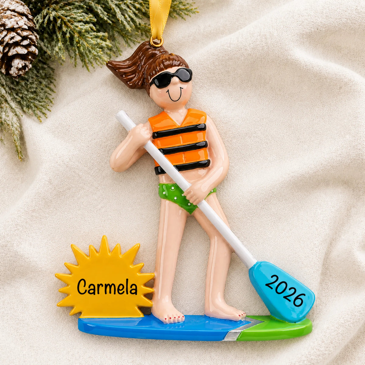 Personalized paddle board girl christmas ornament laid on a soft white knit blanket