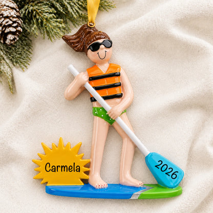 Personalized paddle board girl christmas ornament laid on a soft white knit blanket
