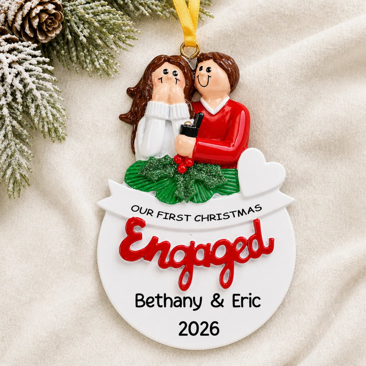 Personalized Our First Christmas Engaged Christmas ornament on a cream knit blanket beside pine and pinecones