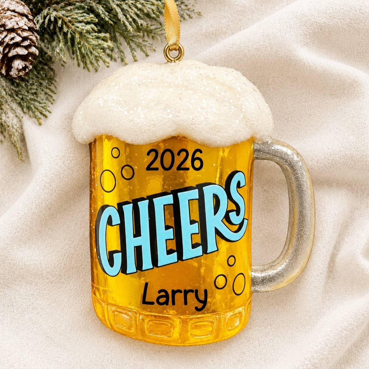 Personalized beer mug Christmas ornament reading Cheers, Larry, and 2026 on a white knit blanket with pine