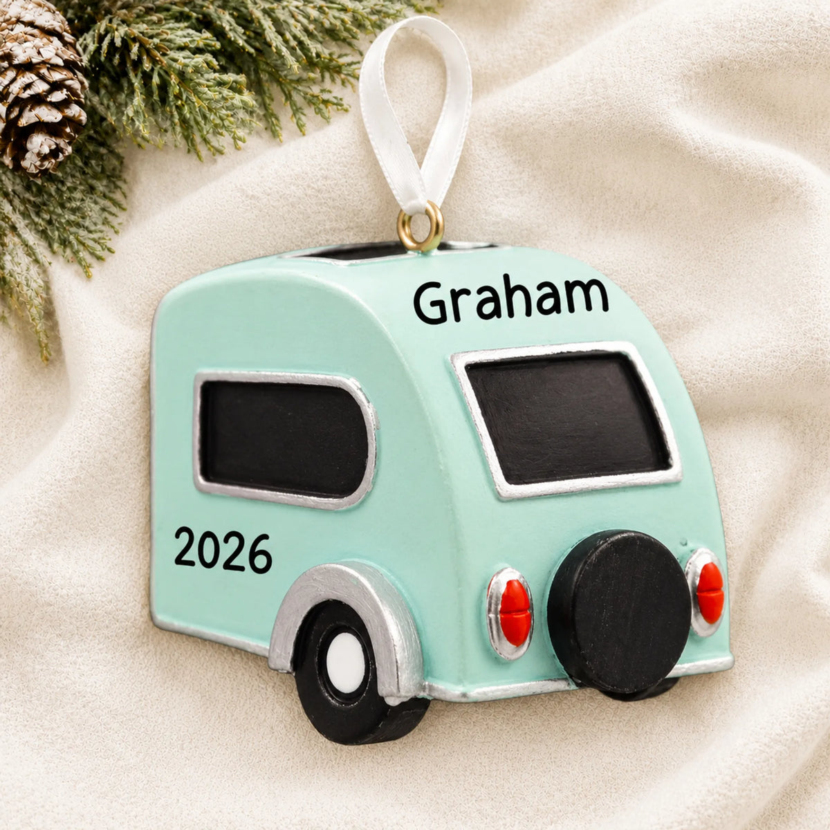 Personalized teardrop camper trailer christmas ornament laid on a soft white knit blanket