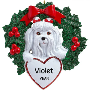 Personalized Maltese Christmas ornament, the Maltese head and paws over a large white heart in a green glitter holly wreath, the pet name and year hand-lettered on the heart