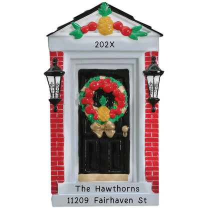 A personalized holiday ornament featuring a red brick home door with a wreath and a pineapple, along with space for names, year, and address.