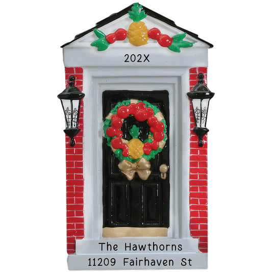 A personalized holiday ornament featuring a red brick home door with a wreath and a pineapple, along with space for names, year, and address.