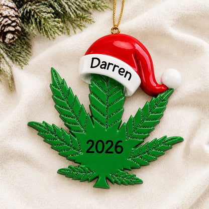 Personalized cannabis leaf santa hat christmas ornament laid on a soft white knit blanket