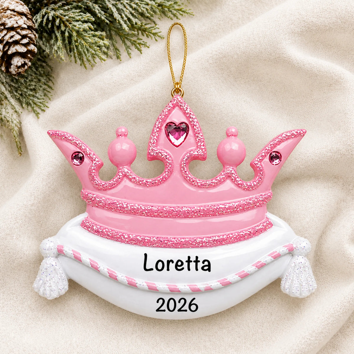 Personalized pink princess crown christmas ornament laid on a soft white knit blanket