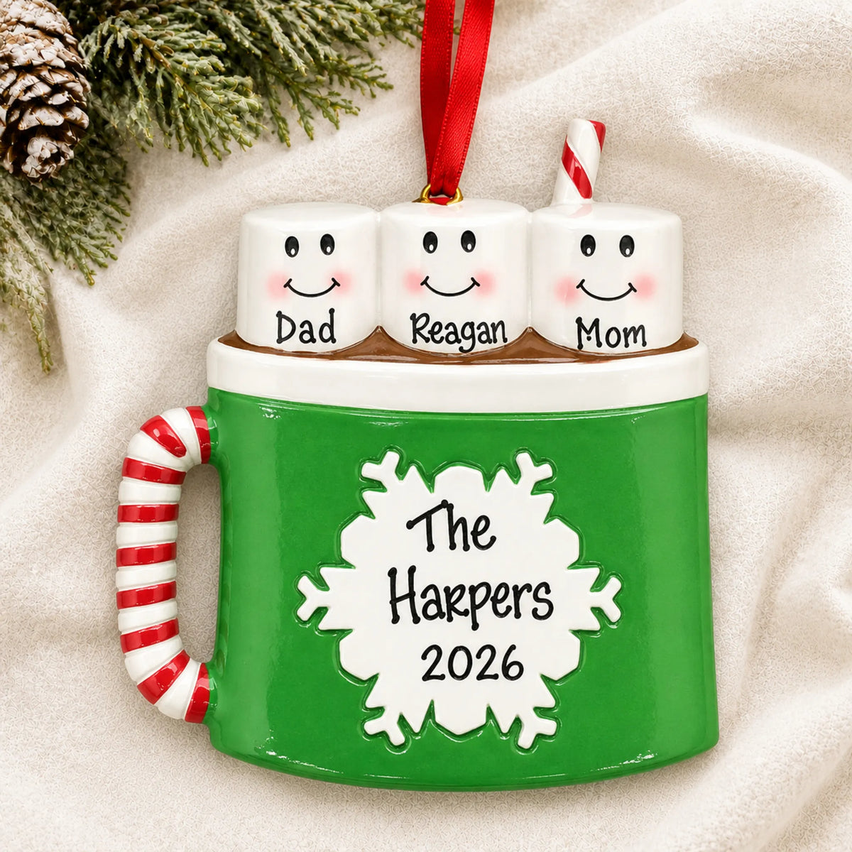 Personalized hot cocoa family of 3 christmas ornament laid on a soft white knit blanket