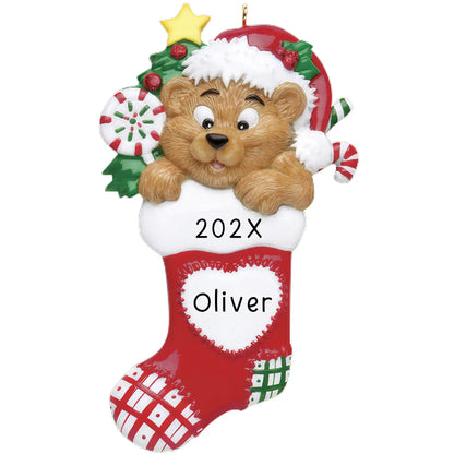 A personalized Christmas ornament featuring a cartoon bear wearing a Santa hat and holding a stocking with a name and year written on it.