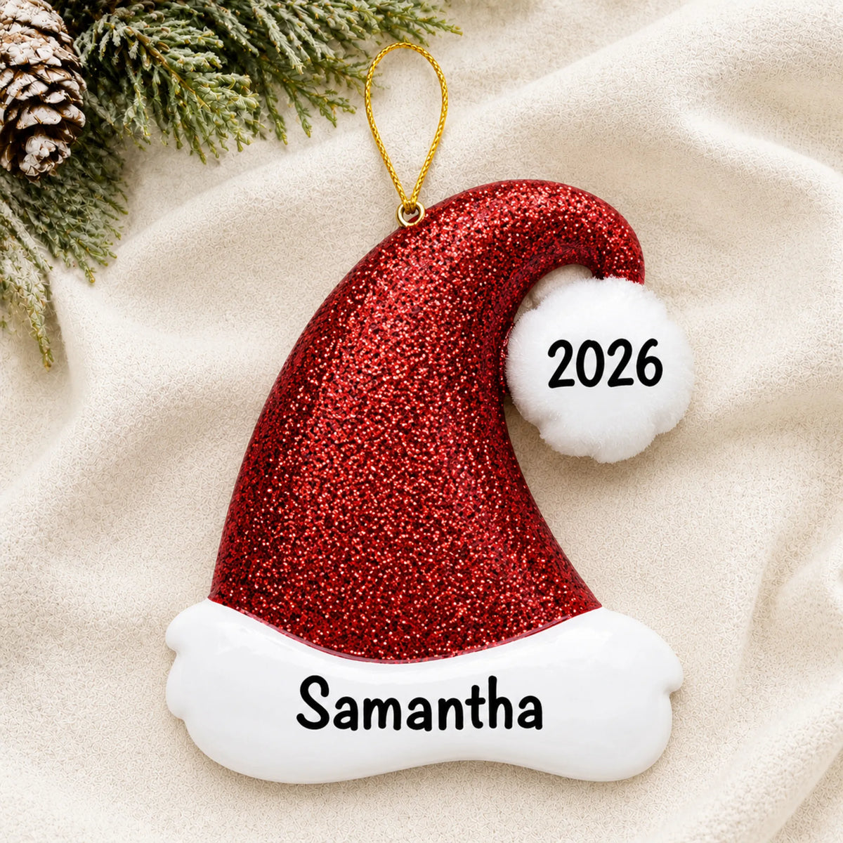 Personalized Santa Glitter Hat christmas ornament laid on a soft white knit blanket