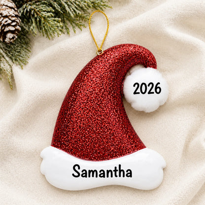 Personalized Santa Glitter Hat christmas ornament laid on a soft white knit blanket