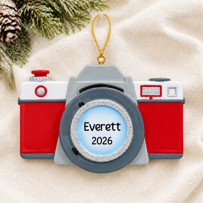 Personalized camera christmas ornament laid on a soft white knit blanket