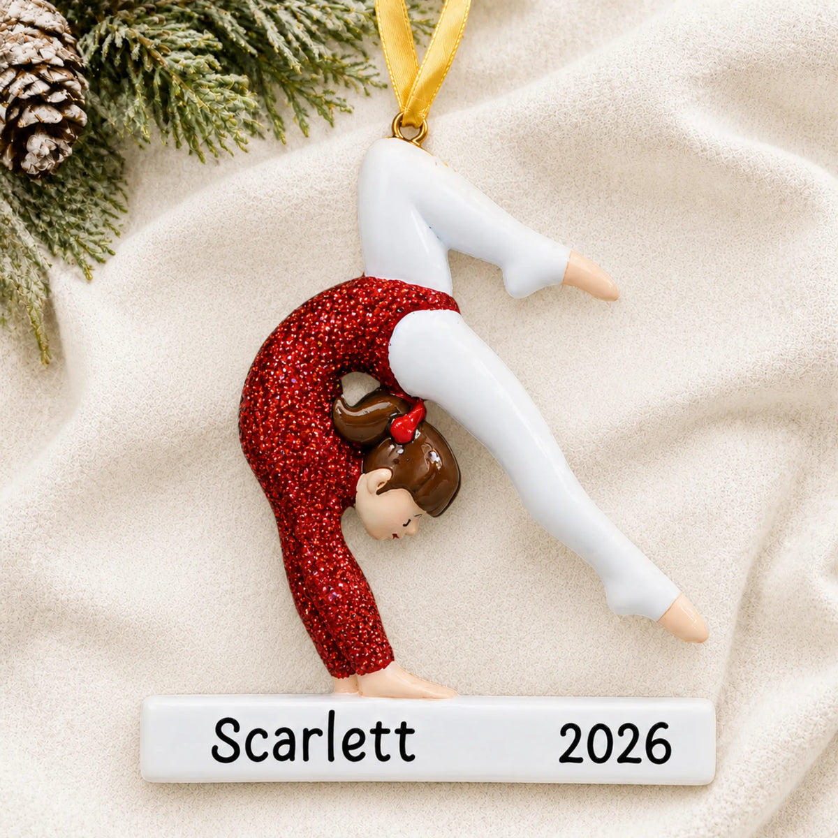 Personalized red glitter gymnastics girl christmas ornament laid on a soft white knit blanket