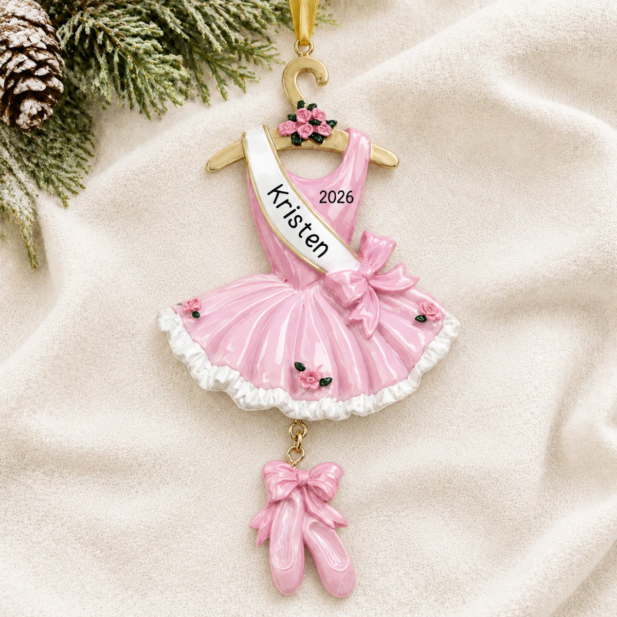 Personalized pink ballerina dress christmas ornament laid on a soft white knit blanket